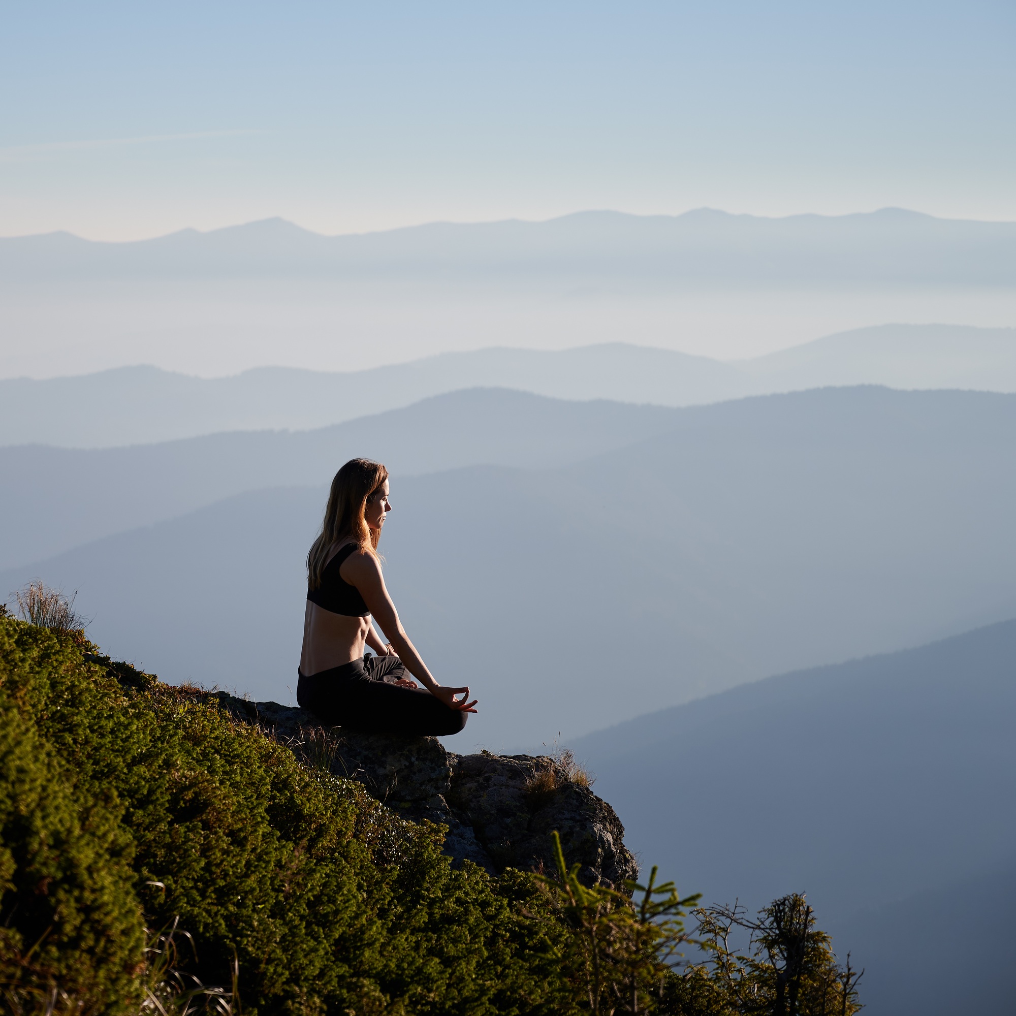Sporty young woman meditating in mountains.