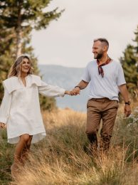 Outdoor shot of young couple in love walking on through grass field in the mountain area